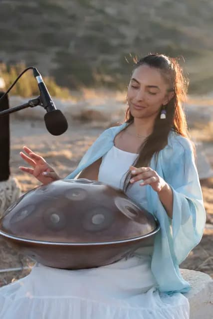 Eyes closed, hands roaming the steel drum — the handpan player lost in the moment in the evening light.