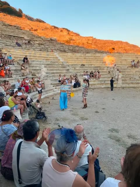 The audience applauds in the ancient theatre of Knidos as models walk the orchestra floor, the upper tiers washed orange by the sunset.