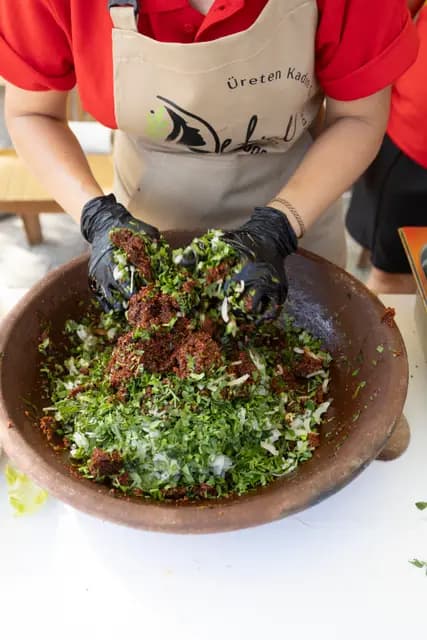 A cooperative member in a “Producing Woman” apron kneads a herbed mixture in a wide earthenware bowl.