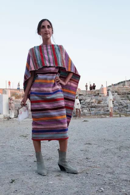 A model walks the runway in a striped handwoven set, the ancient wall behind.