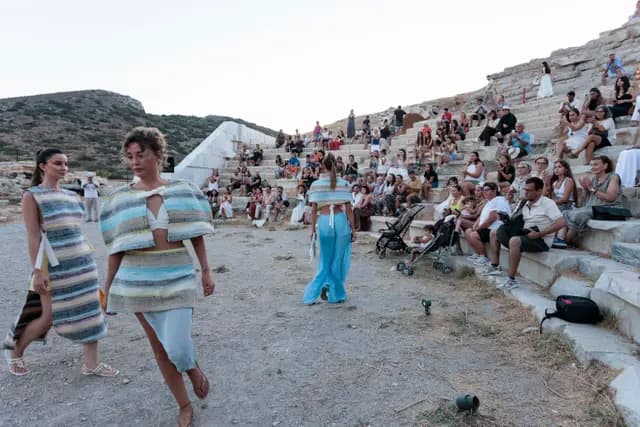 Two models walk in front of the audience filling the steps of the ancient theatre.