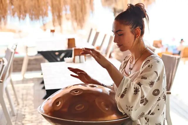 A young musician plays the handpan on the beach stage, hands suspended above the instrument.