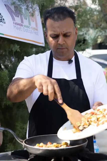 The chef slides chopped vegetables from plate to pan — the cooking moment caught at its peak.