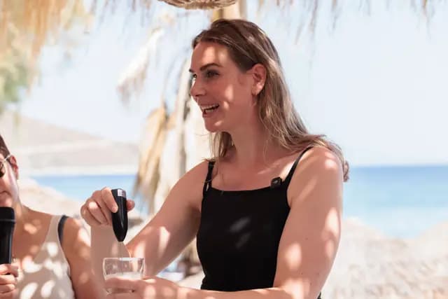 A workshop guest pours the mixture into a glass with a hearty laugh, the sea opening up behind.