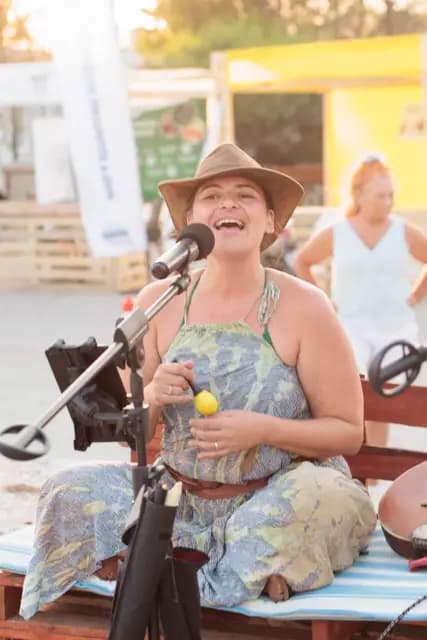 A musician in a straw hat sings with a shaker in hand, close to laughter in the evening light.