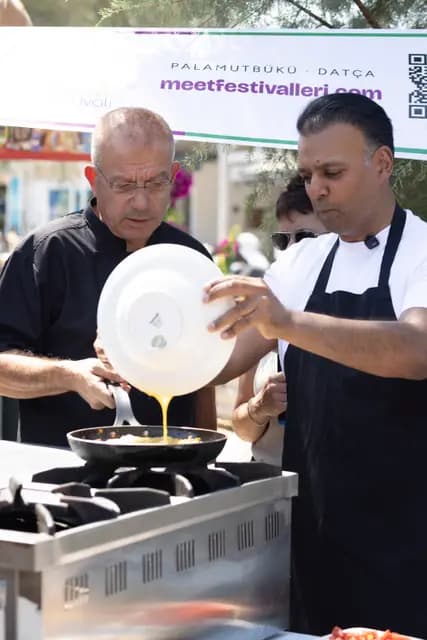 Two chefs work together, pouring egg from plate to pan in one clean, visible line.