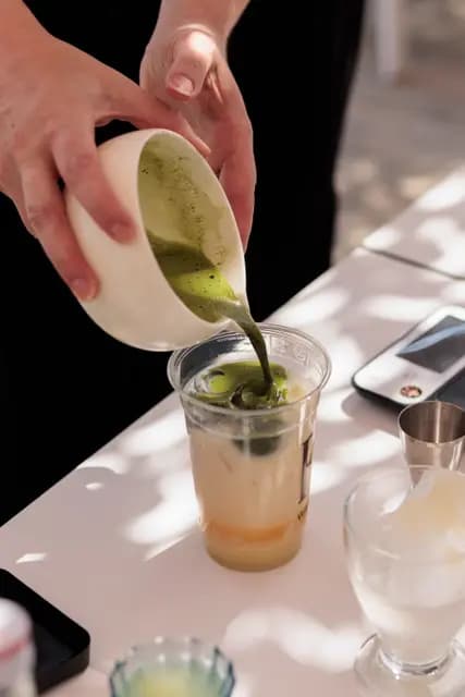 Hands pour matcha into an iced glass — the workshop's result in close-up.