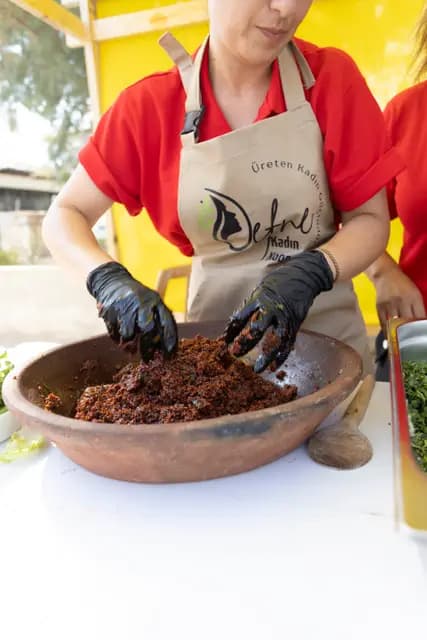 A producer with the cooperative logo on her apron kneads the mixture in an earthenware pot.
