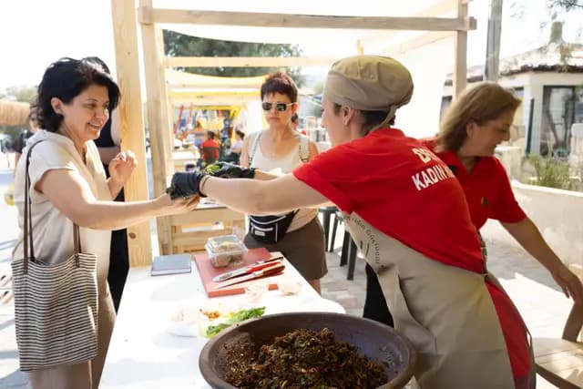 A cooperative member in a red shirt offers a taste to a visitor, a genuine smile on her face.