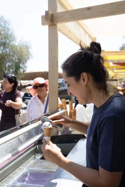 An ice cream maker carefully fills a cone while the queue watches with curiosity.
