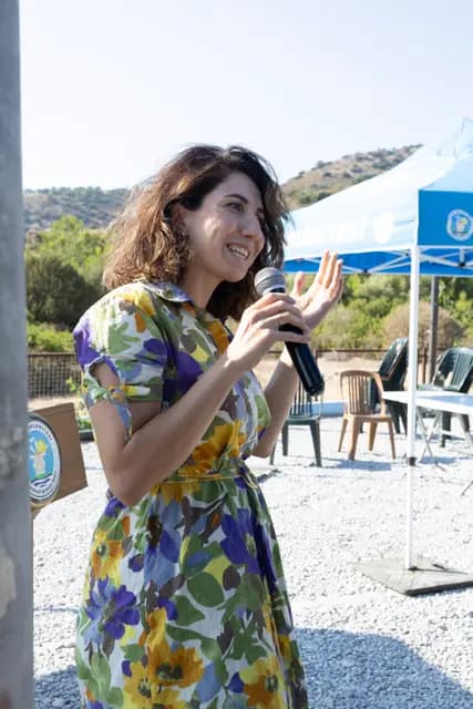 A speaker in a floral dress raises her hand as she addresses the audience on the microphone.