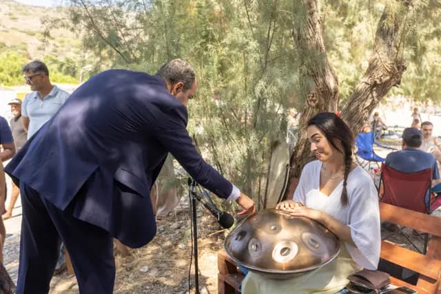 An official leans in to touch the handpan while the young musician watches with a smile.