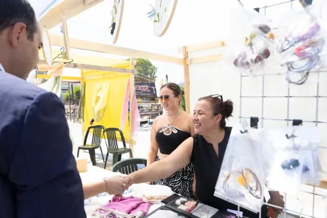 At the handmade jewellery stand an official shakes hands with two women producers, who greet them with laughter.