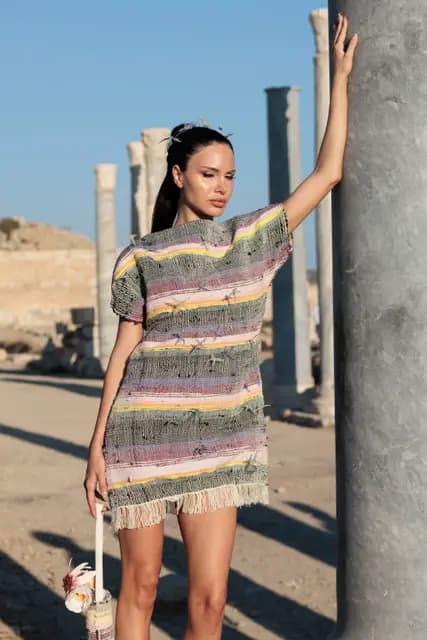 Hand resting on an ancient column, a model in a tasselled woven dress stands before the colonnade of Knidos.