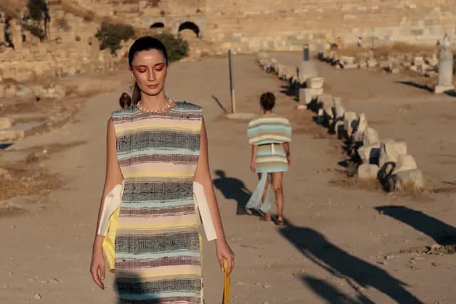 A model in a striped woven dress with the colonnaded ancient road and a second model stretching out behind her.