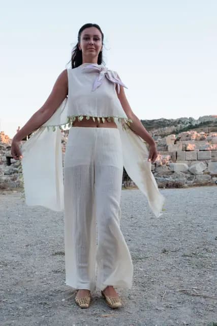 In a cream linen suit, a model opens her arms to show how the fabric falls, her gaze straight at the camera.
