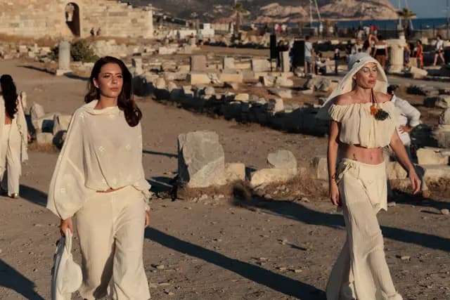 Two models in cream suits walk side by side, the one in front looking straight at the camera.