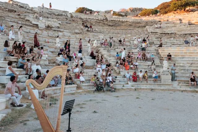 The audience spread across the stone tiers of the ancient theatre, the harp in the foreground giving the recital its scale.