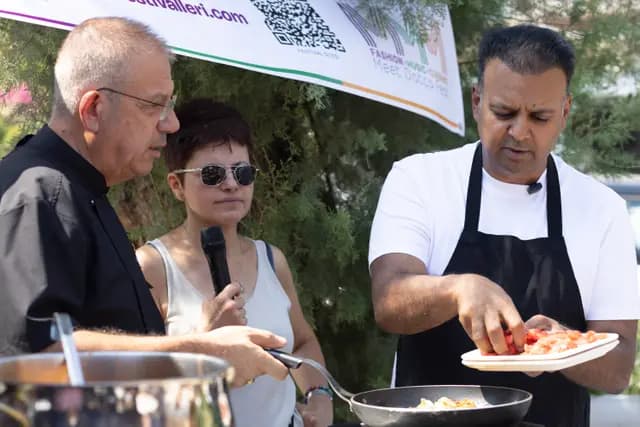 Two chefs work side by side at the stove while the host narrates on the microphone.