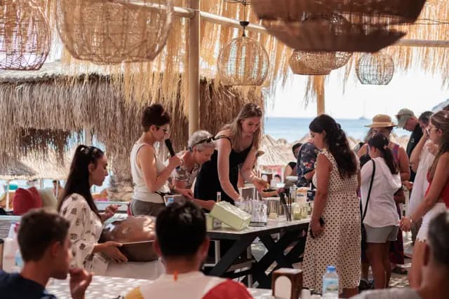 The workshop table under the reed canopy with the crowd around it, Palamutbükü bay behind.