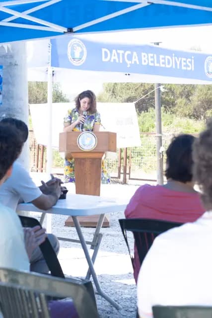 The host opens the day's programme at the lectern, the municipal canopy behind her.