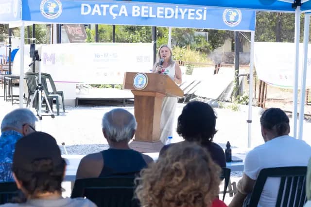 A speaker addresses the audience from the lectern while those in the front row take notes.