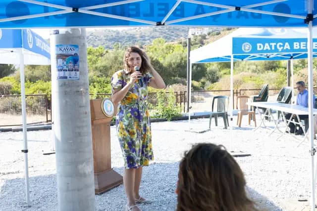 The host in a floral dress introduces the next part of the programme in front of the lectern.
