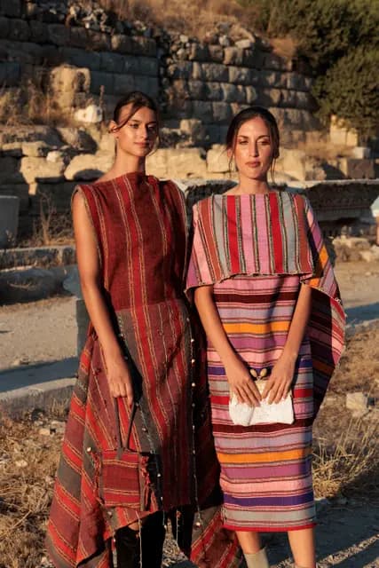 Two models in cream linen walk the ancient road, their shadows stretched long.